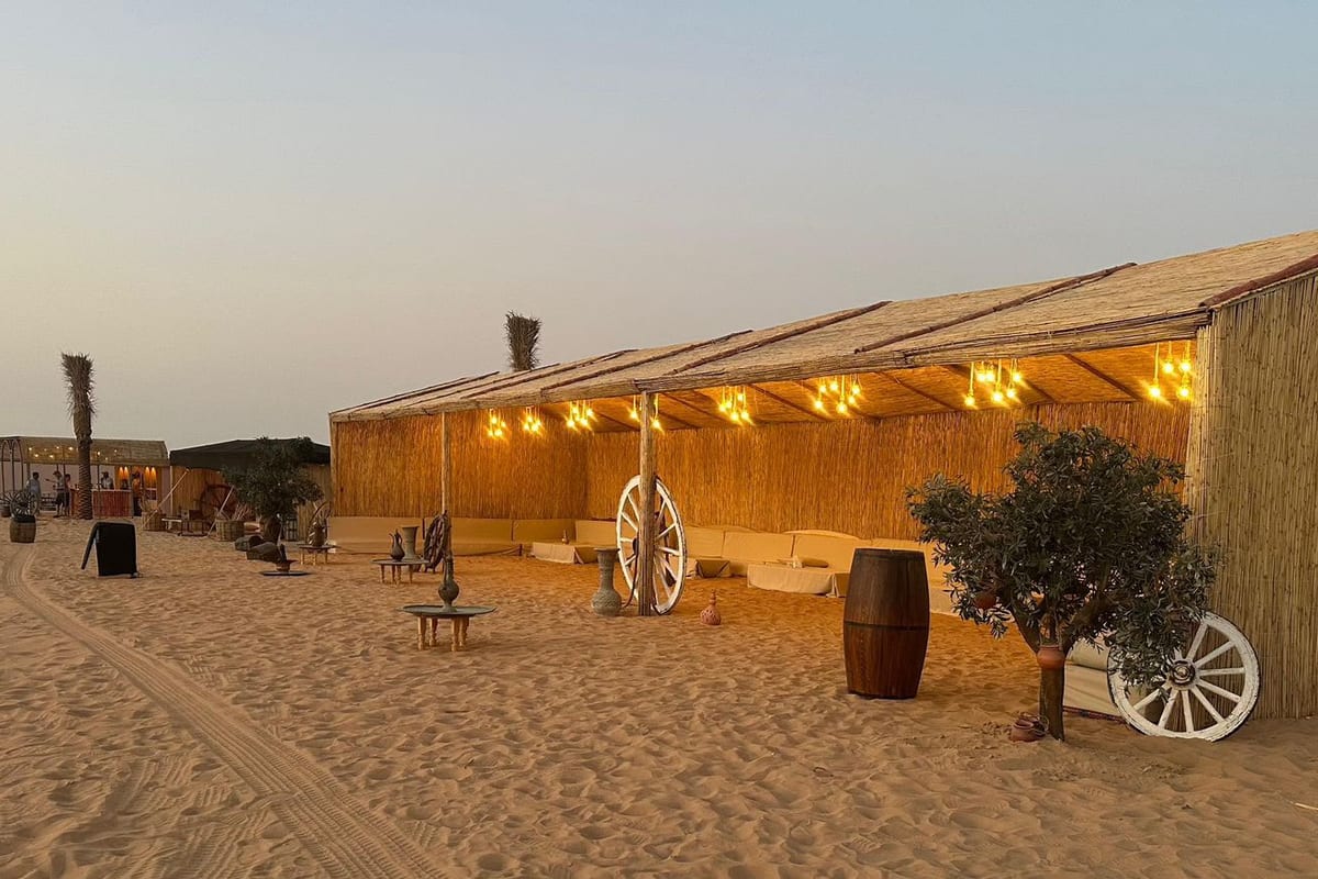 Reed huts and a wagon-wheel decoration at the Lahbab desert camp at dusk