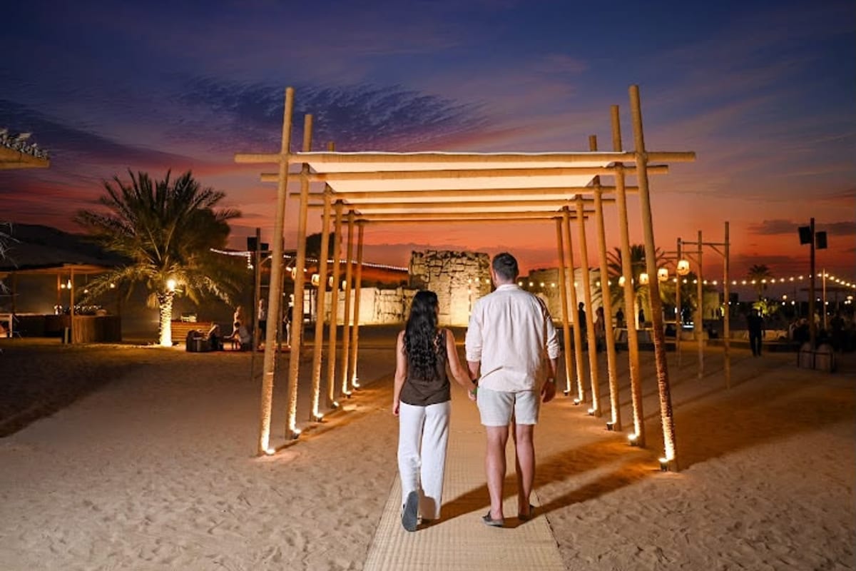 Couple walking into the desert camp under a lit pergola at dusk