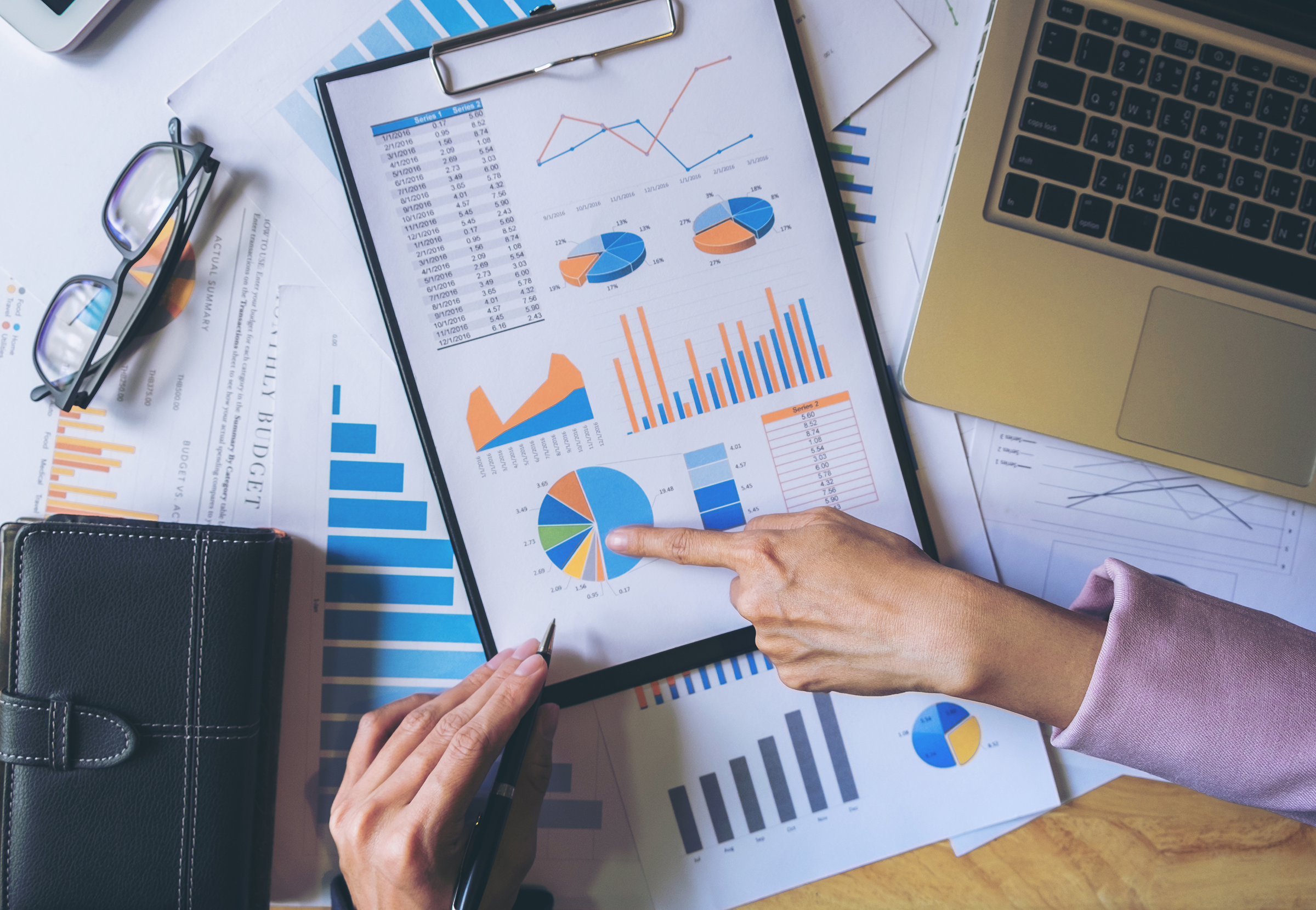 A business professional points to a clipboard of pie charts, bar charts, line graphs, and data.