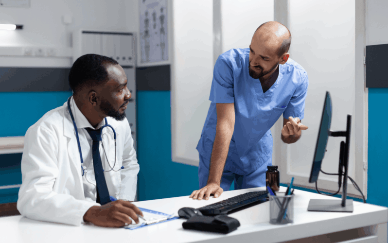 A doctor and nurse speaking with one another inside a medical office