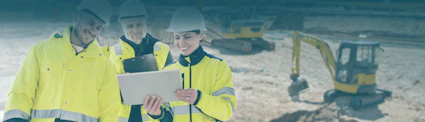 Frau mit gelber Jacke, Bauhelm und Tablet vor Baustelle mit gelben Baggern