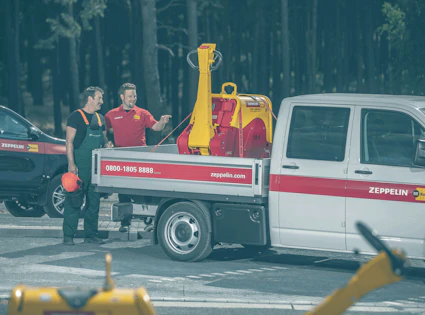 zwei männer beladen transportauto mit rüttelplatte