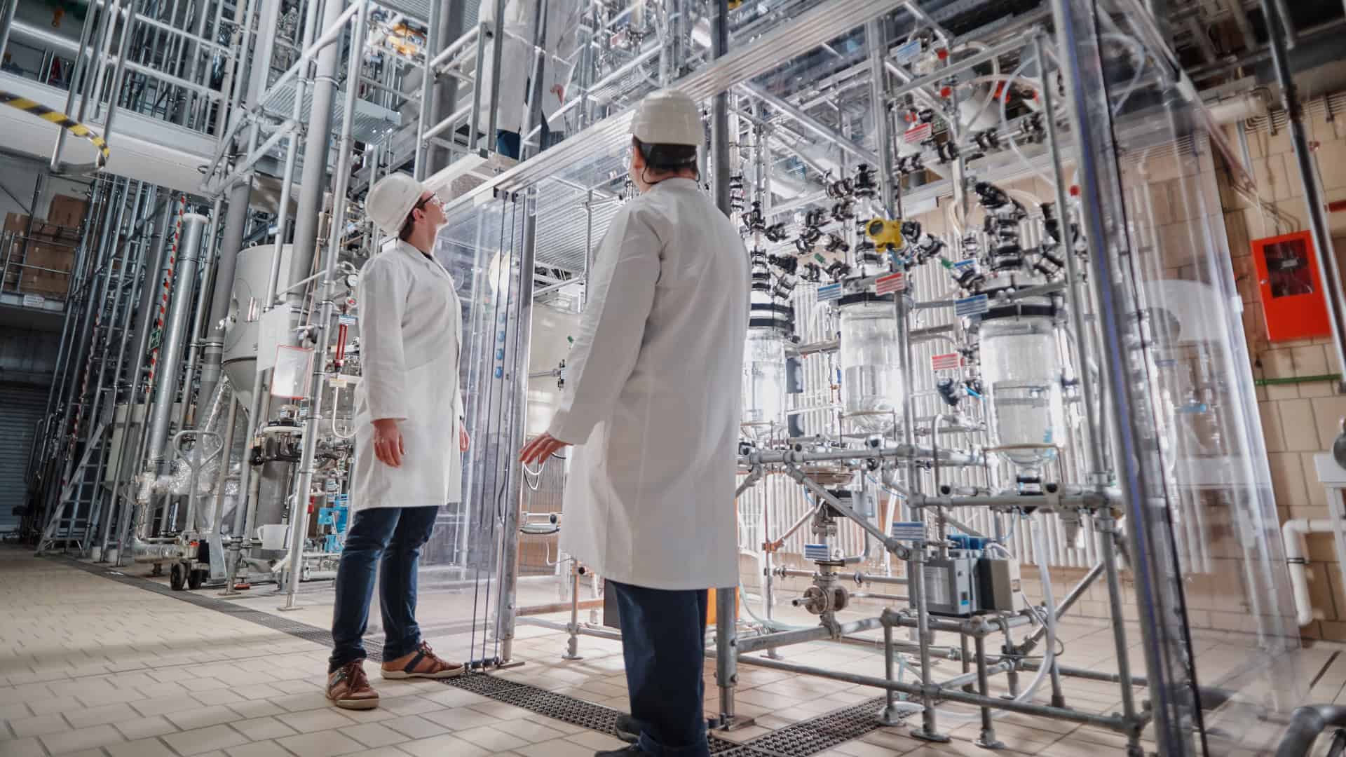 Innovative chemical engineering lab with researchers in white coats and safety helmets exploring complex industrial machinery.