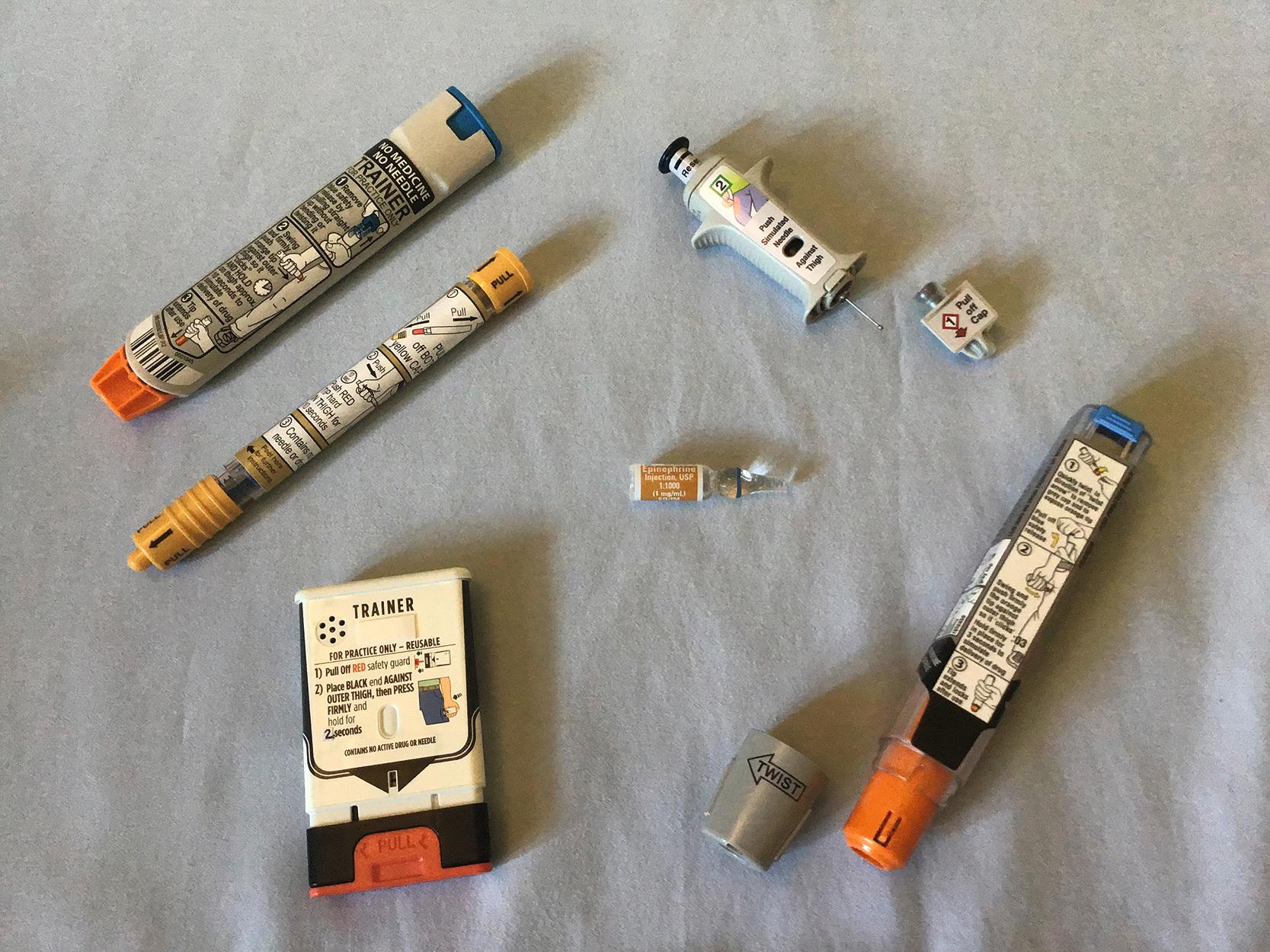 Fig. 4.5, Currently available automated epinephrine injector devices as compared to a glass ampule of epinephrine (1 mg/1 mL) solution in center.