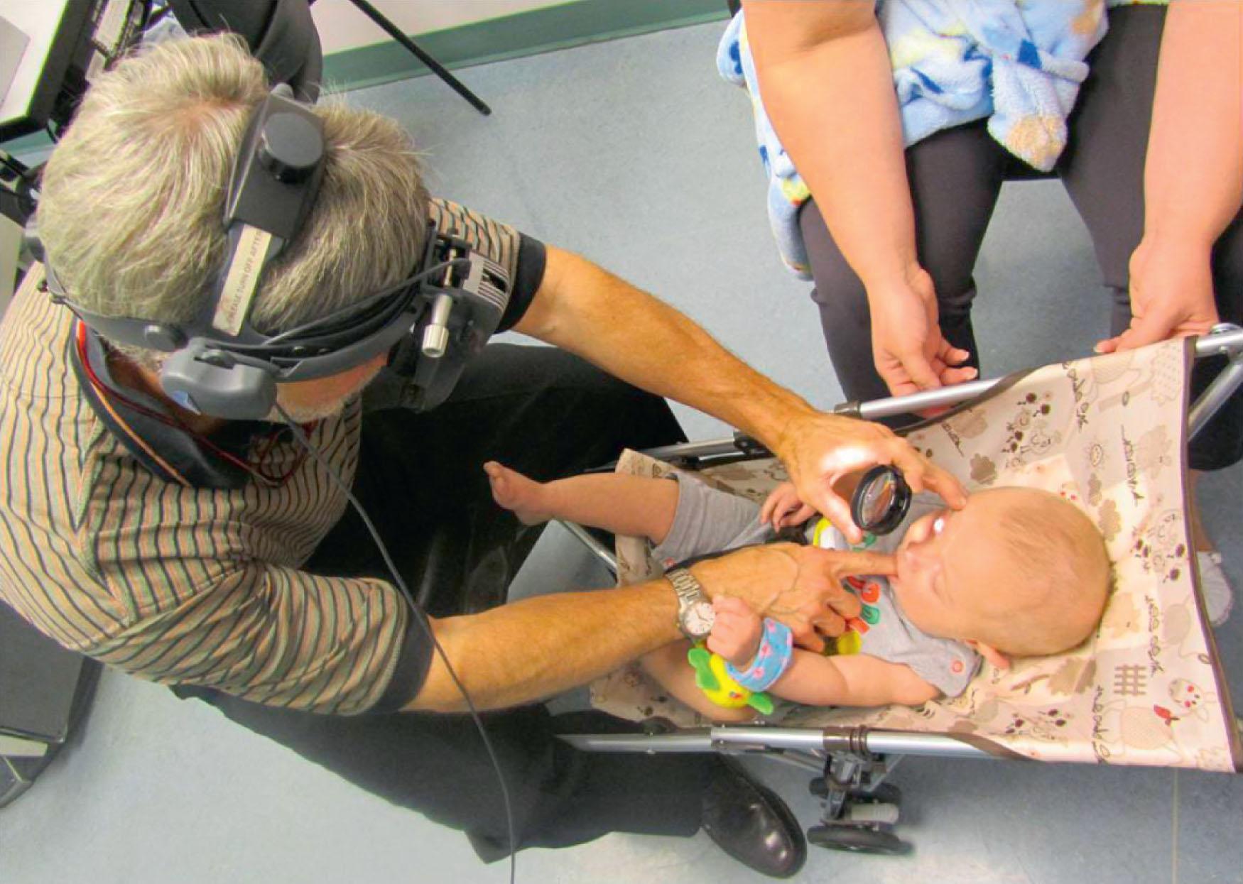 Fig. 5.2, Indirect ophthalmoscopy in infants. An example of unconventional assessment techniques necessary in infants. Here the examination is carried out successfully in the patient’s own comfort zone: a stroller and a good suck on the examiner’s finger.