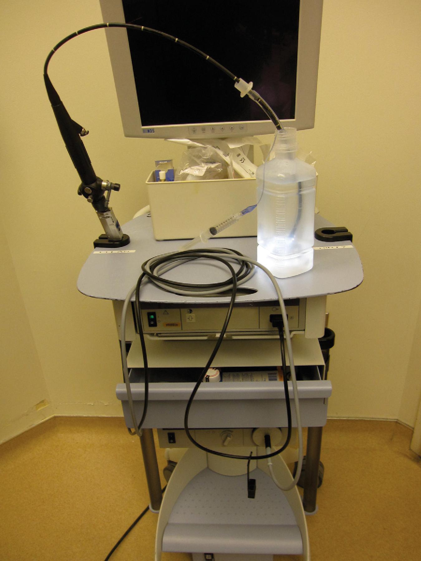 Fig. 24.8, Mobile airway cart with a video screen and supplies underneath. The flexible intubation scope (FIS) is braced in the clean container on the left, and a holding tube for the used FIS is located on the right. The FIS insertion section lies within an endotracheal tube in a warm saline solution.