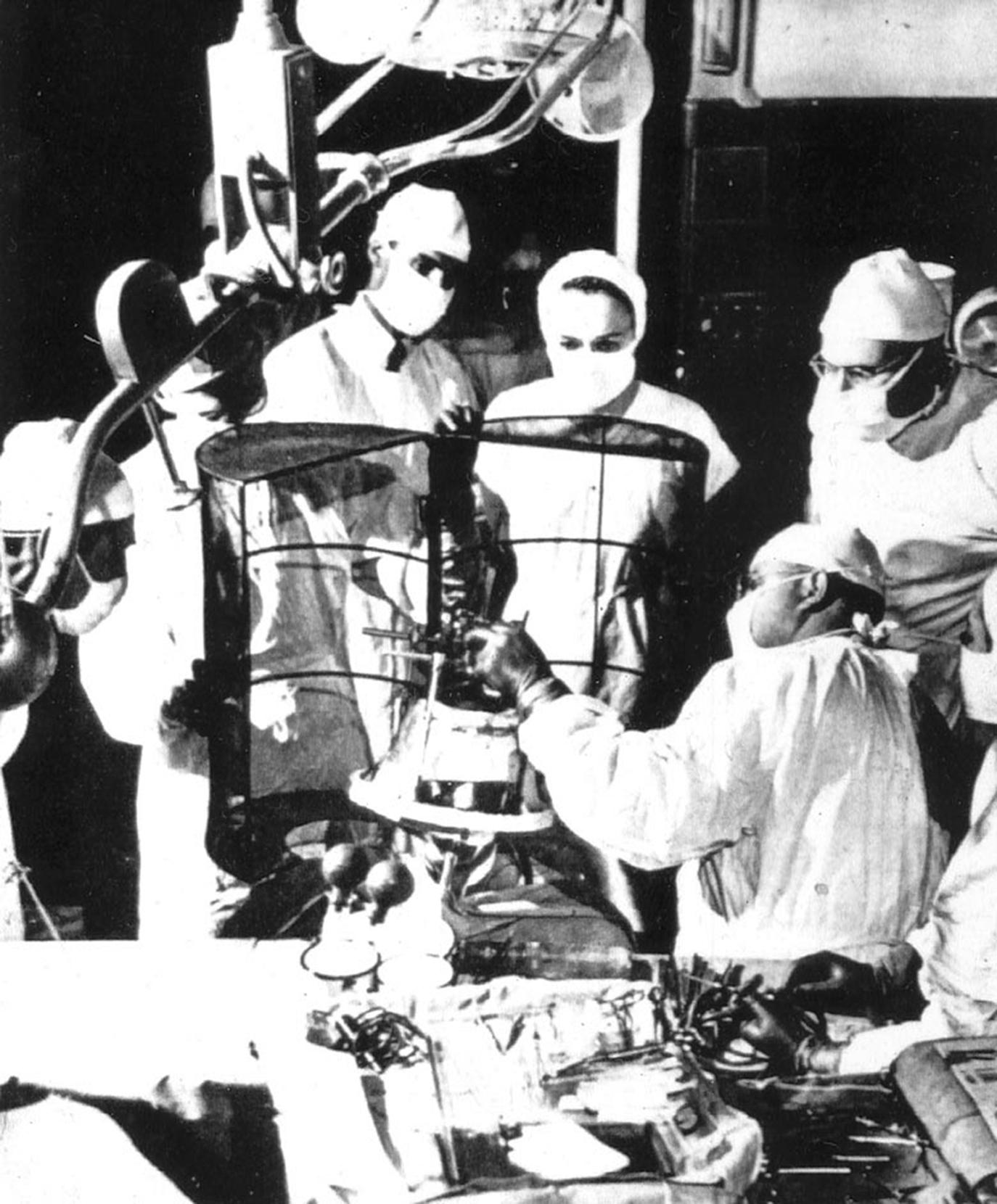 Figure 120.4, Photograph of Spiegel and Wycis in the operating room. The Faraday cage, for electrical shielding, is a cylindrical enclosure that opens along the long axis.