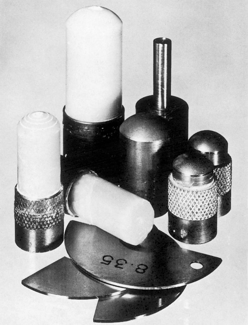 Fig. 33.4, Left to right: (rear) large wax tool and spindle lens holder (or edging chuck); (centre) small wax tools, cut and uncut, and large and small diamond-impregnated brass tools; (front) female gauges.