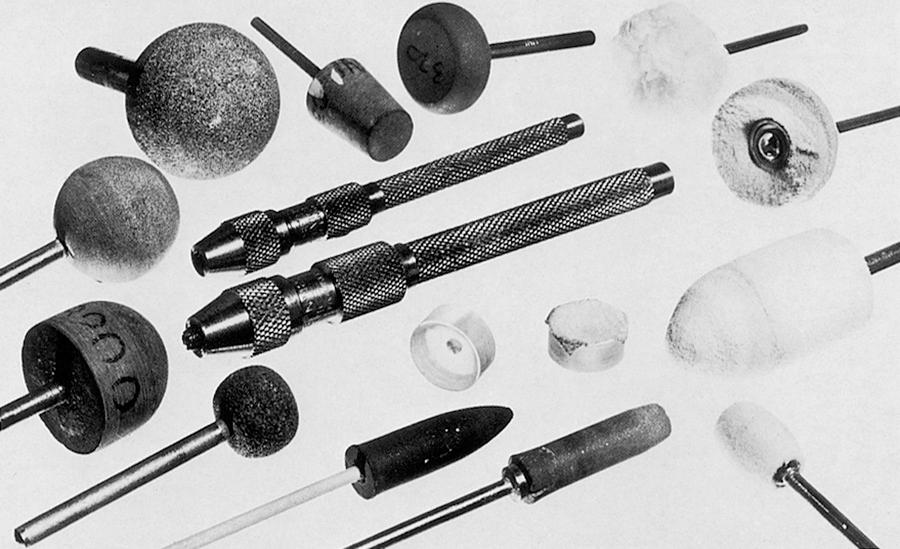 Fig. 33.6, Assorted grinding tools and polishing buffs. Top centre: large and small pin-vice holders for drills. Lower centre: corneal lens buttons with one surface cut for use as scleral lens runners. The left button shows a guide hole on the rear surface; the right button has double-sided adhesive tape on the concave surface.