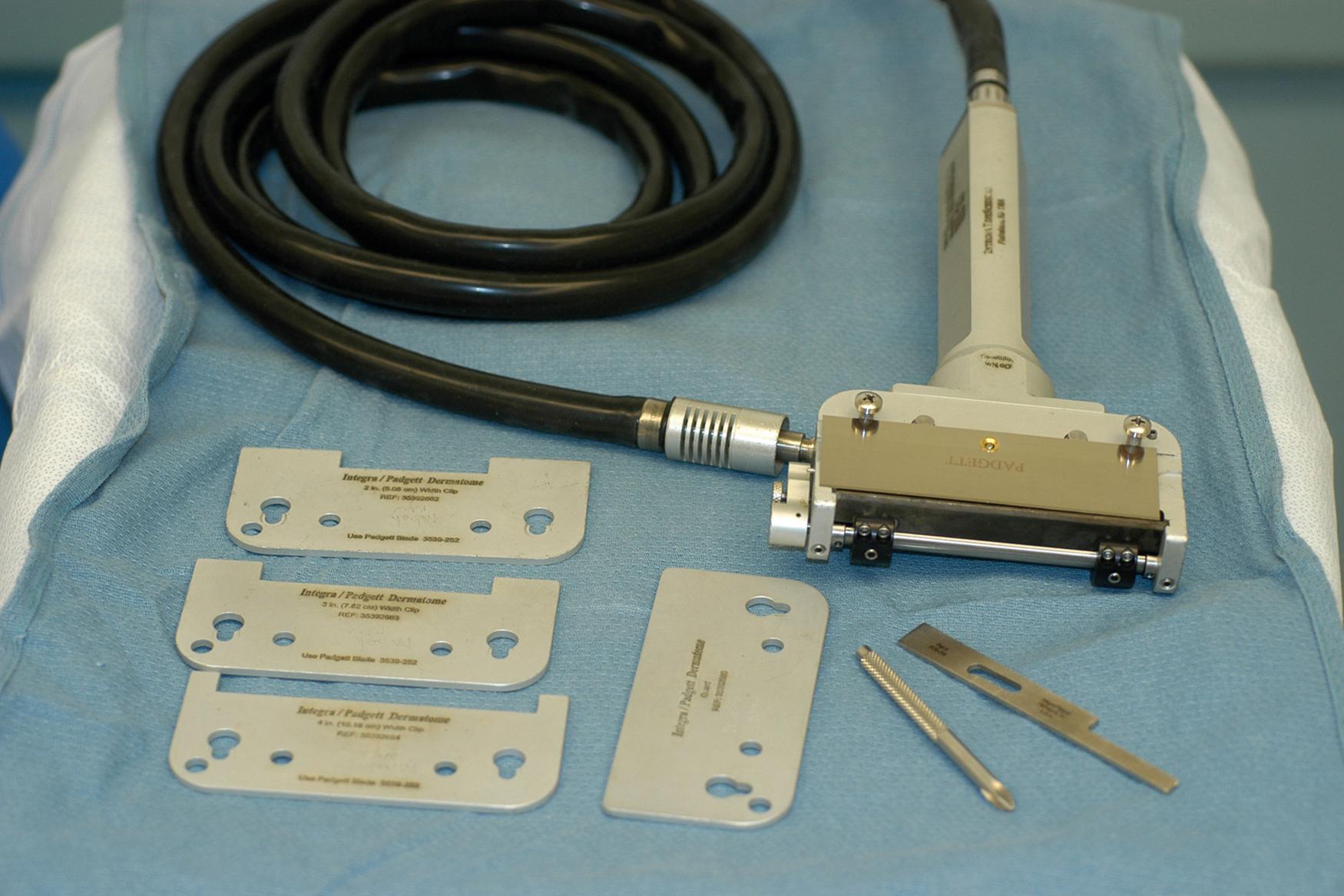 Fig. 44.5, The Padgett gas-turbine-driven dermatome. Guards are shown on the lower left with variable openings to control the width of the graft. The blade is seen loaded on the device.