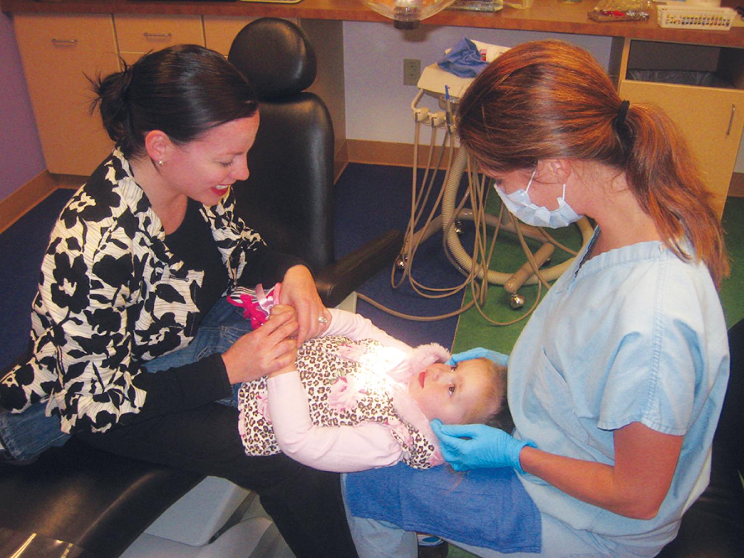 Fig. 21.1, Oral examination of a toddler. A lap examination is a useful way to examine a young or anxious child. The patient is able to hold the parent’s hand and see the parent during the examination.