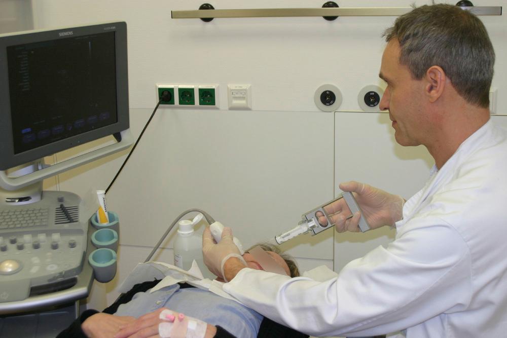 Fig. 3.2.13, Setting for interventional ultrasound: the area of interest of the patient is situated between the examiner and the ultrasound screen. The direction of view and manipulation are the same and the examiner does not have to turn around. The plane of the ultrasound and the direction of the needle are parallel (“long axis” technique). A handle for aspiration is used.