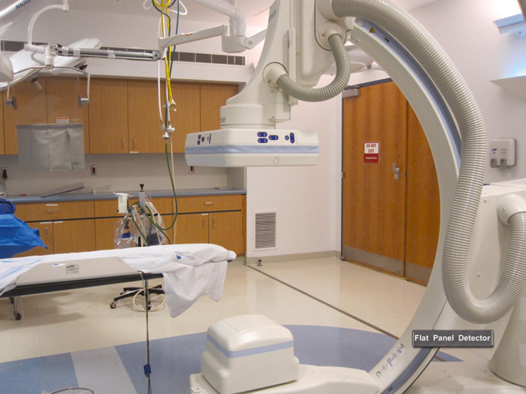 Figure 2.1, A representative cardiac catheterization laboratory. The x-ray tube is located below the table, and the flat-panel detector is located above the table, both mounted on a C arm. Shielding, image monitors, and emergency equipment can also be seen.