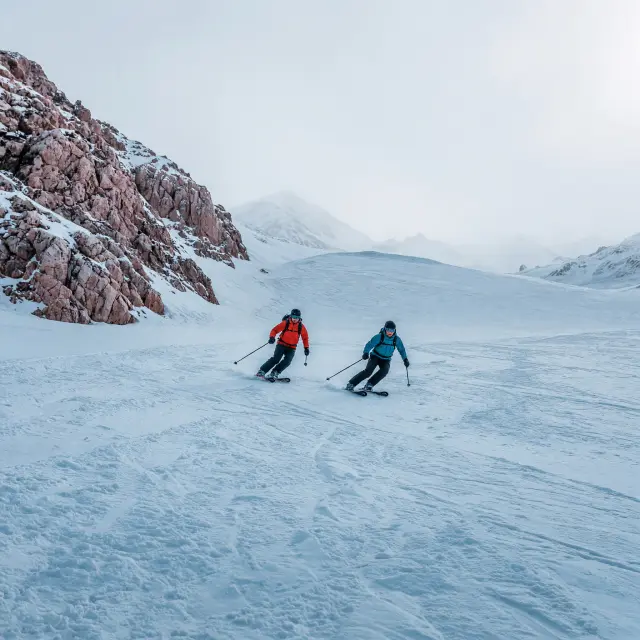 Besneeuwde gletsjer en rotswand van de Marmolada in de Dolomieten onder een heldere blauwe lucht met skiërs