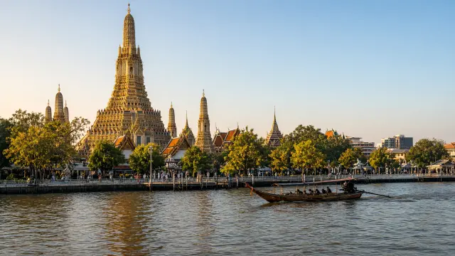 Tempel aan de rivier in Bangkok met een longboat in de namiddagzon