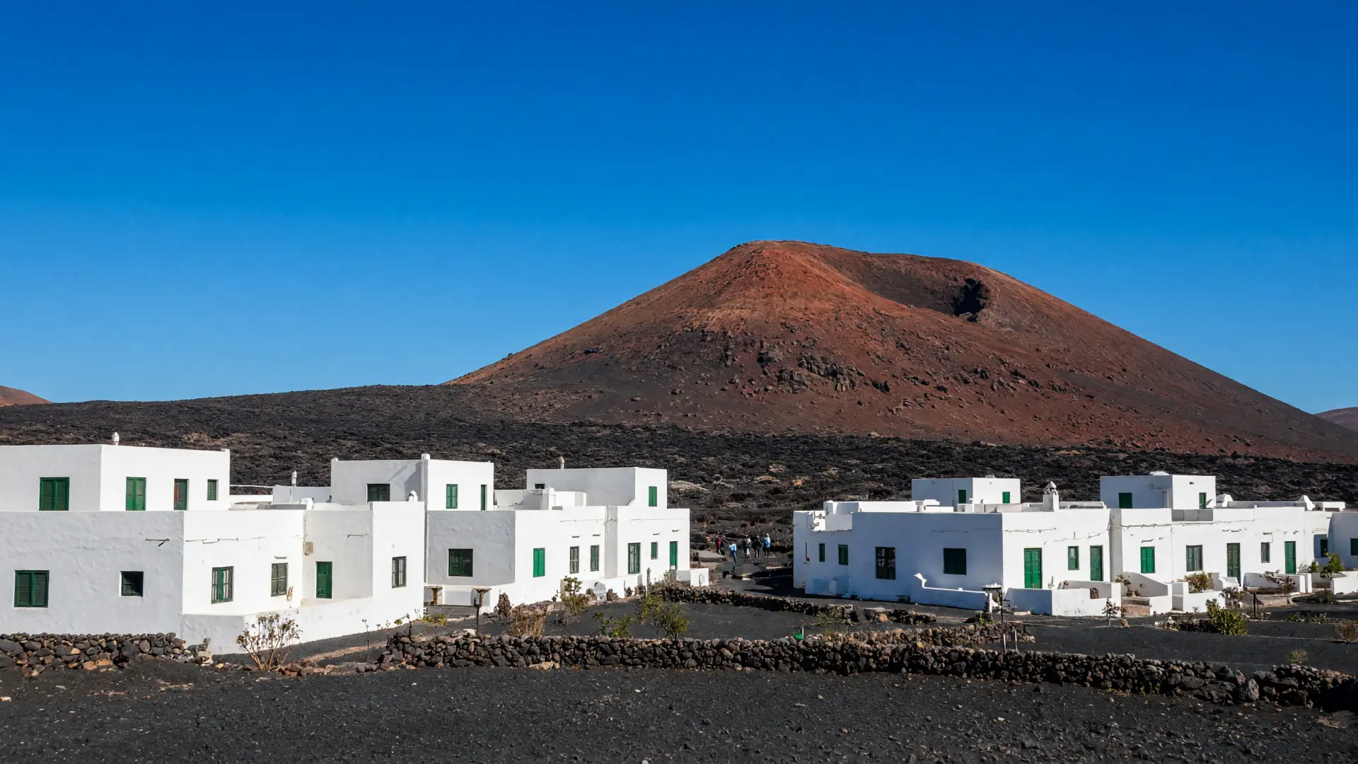Wit dorp met groene luiken en een vulkaan op de achtergrond op Lanzarote