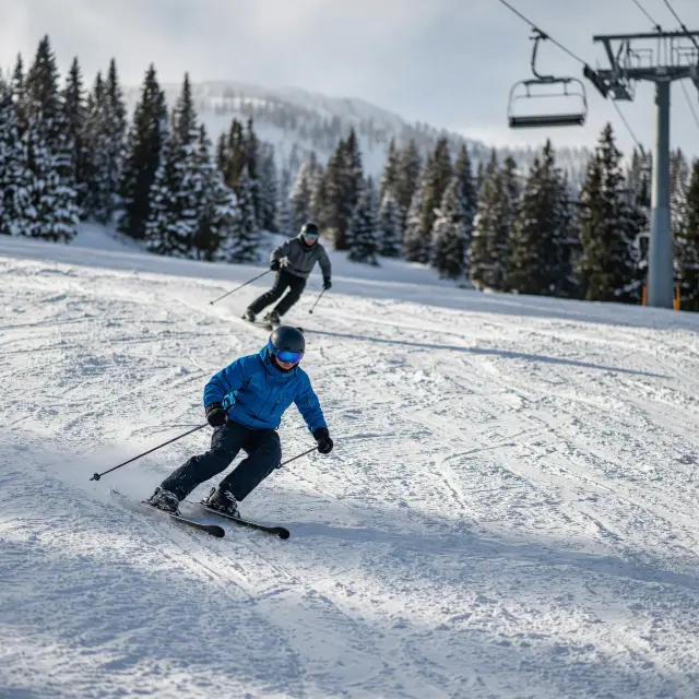 Skiërs op een brede piste met uitzicht op besneeuwde bergtoppen in de Franse Alpen
