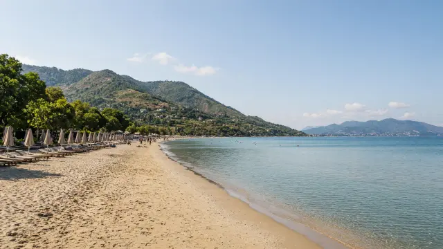 Lang zandstrand met parasols aan de noordkust van Corfu met groene bergen erachter