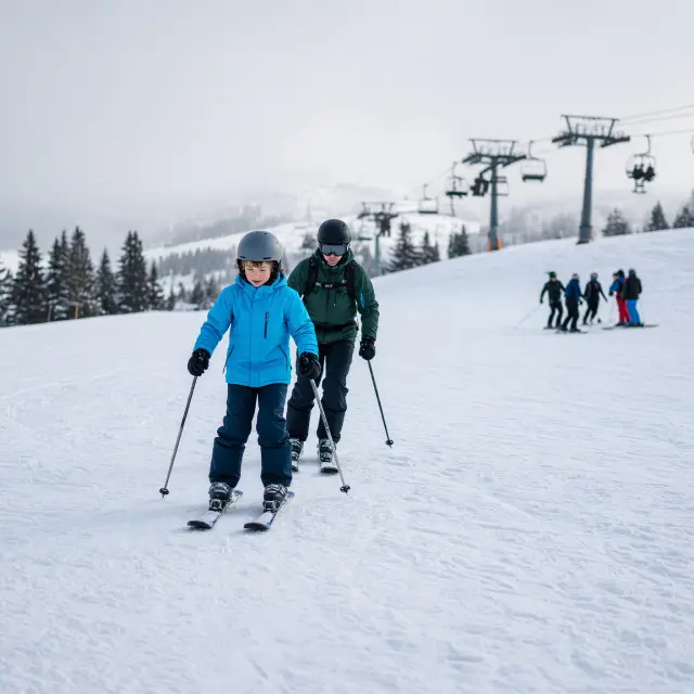 Beginnende skiërs en kinderen op een brede blauwe piste in Westendorf met bergen op de achtergrond