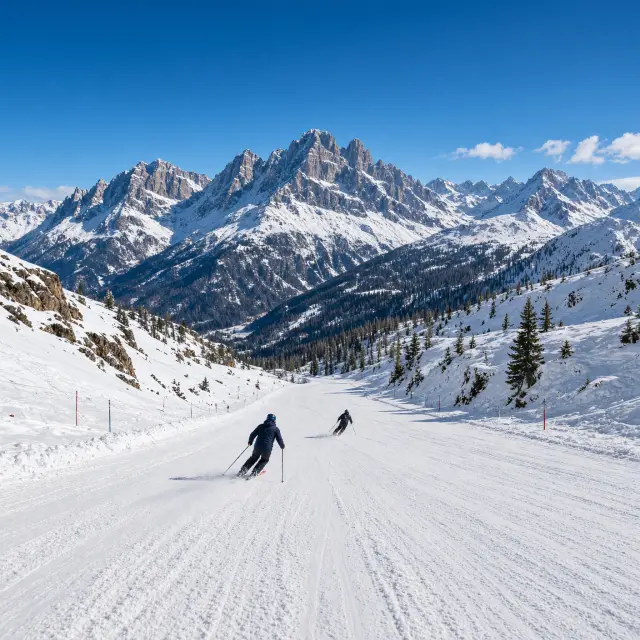 Skiërs dalen af op een brede, zonnige piste met uitzicht op de bergtoppen van de Brenta-Dolomieten