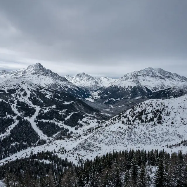Skiers carving down pristine snowy slopes in the French Alps with dramatic mountain peaks and blue skies, perfect for last minute skivakantie Frankrijk