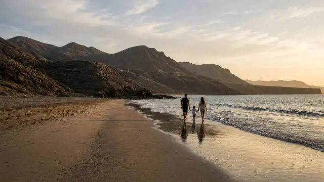 Gezin wandelt in de namiddagzon langs de waterlijn van een warm strand met heuvels op de achtergrond