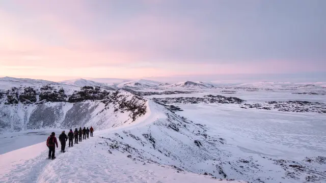 Wandelaars op sneeuwschoenen op de kraterrand van de Hverfjall boven het bevroren meer Mývatn