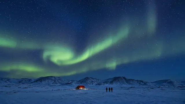 Groen noorderlicht boven een besneeuwd landschap in IJsland met een verlichte boerderij