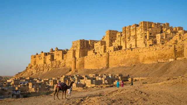 Het zandstenen fort van Jaisalmer in Rajasthan met een kameel en enkele mensen op de weg ervoor