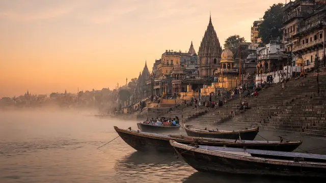 Roeiboten op de Ganges bij de ghats van Varanasi bij zonsopgang, met pelgrims op de trappen