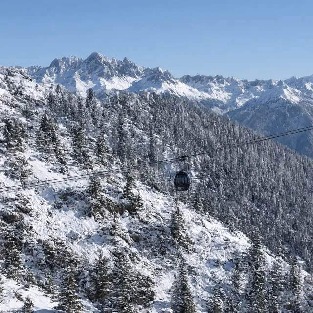 Skiërs op een brede rode piste met moderne gondellift in de achtergrond omringd door besneeuwde Alpentoppen
