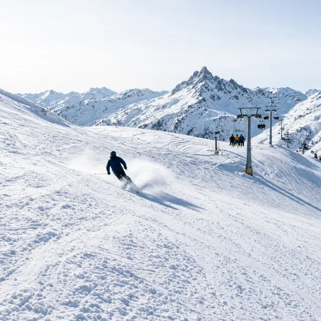 Skiers dalen af op een brede, zonnige piste in het hooggelegen Silvretta-skigebied boven Ischgl