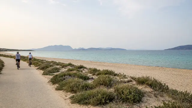 Fietsers op een kustpad langs een breed zandstrand met duinen bij Tigaki op Kos