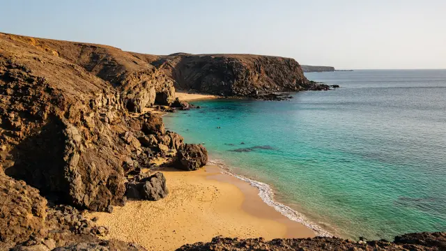 Beschutte baai met goudgeel zand tussen vulkanische kliffen bij Papagayo op Lanzarote