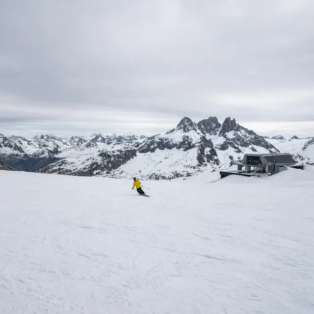 De Glacier de Mantel in Les 2 Alpes met moderne gondellift en skiërs op brede blauwe pistes tegen een achtergrond van de Écrins