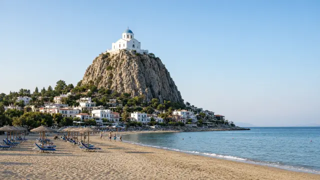 Wit kerkje boven op een hoge rots in het dorp Petra op Lesbos, met een zandstrand ervoor