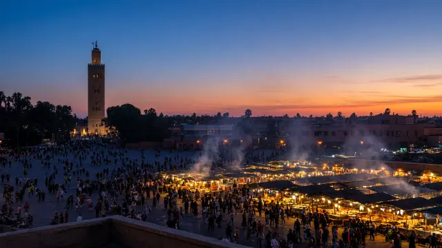 Het plein Djemaa el-Fna in Marrakech bij schemering, met rokende eetkraampjes en de Koutoubia-minaret