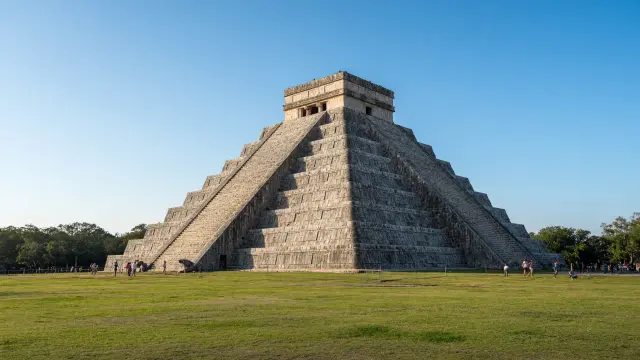 De piramide El Castillo in Chichén Itzá in het ochtendlicht, met kleine bezoekers op het grasveld