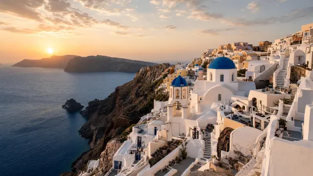 Witte grotwoningen en een kerk met blauwe koepel op de rand van de caldera in Oia op Santorini bij zonsondergang