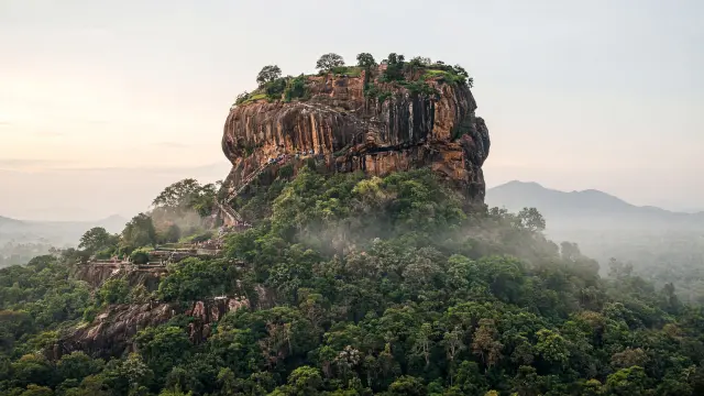 De Leeuwenrots van Sigiriya boven de groene jungle, met kleine bezoekers op de trappen
