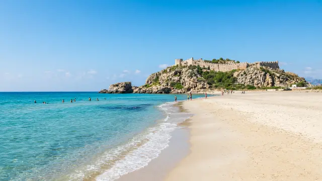 Lang zandstrand met helder water aan het Kleopatrastrand in Alanya met de burcht op de achtergrond