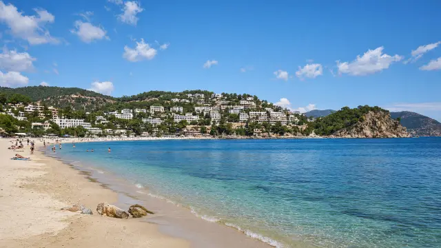 Zandstrand in een baai bij Kusadasi met witte hotels op de groene heuvels