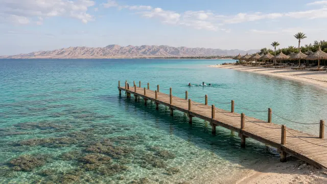 Houten steiger boven helder turquoise water en koraalrif aan de Rode Zee in Egypte, met woestijnbergen op de achtergrond