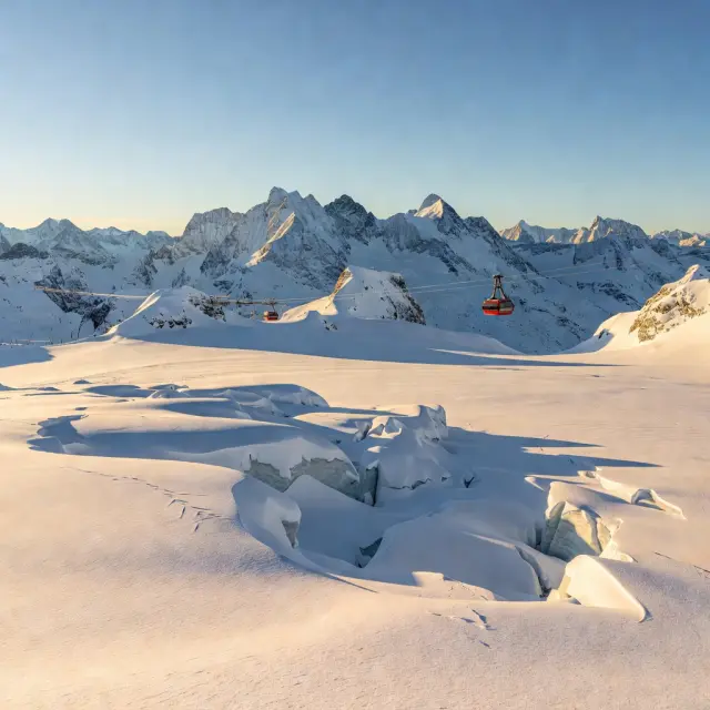 Bergstation van de 3K K-onnection gondel op de Kitzsteinhorn gletsjer met skiërs op brede gletsjerpistes onder blauwe hemel