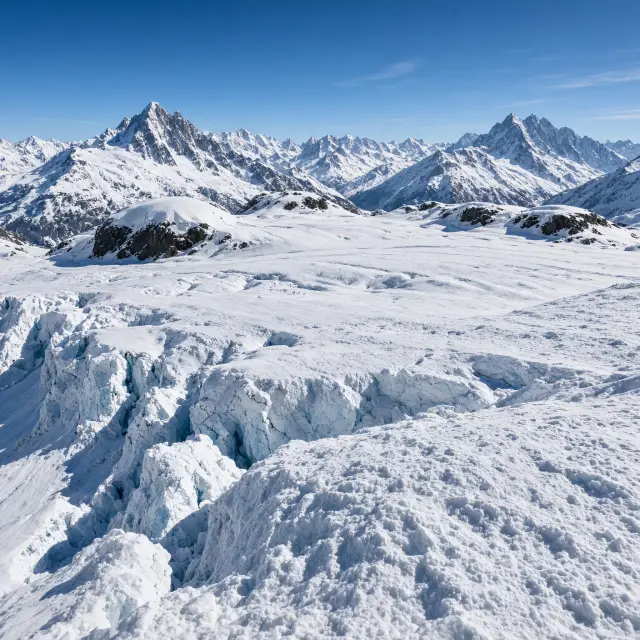 Spectaculair uitzicht op de Zwitserse Alpen met besneeuwde bergtoppen, gletsjer en skiërs op hoogalpiene pistes onder strakblauwe hemel