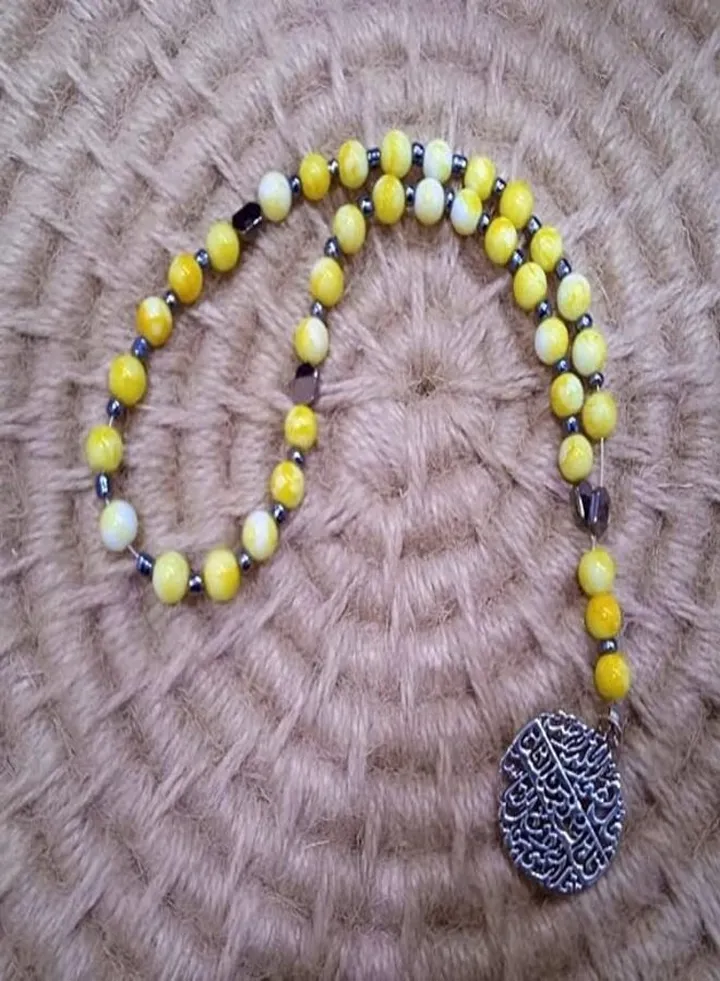 A rosary of 33 yellow beads, decorated with spacers of black beads, with a silver religious pendant