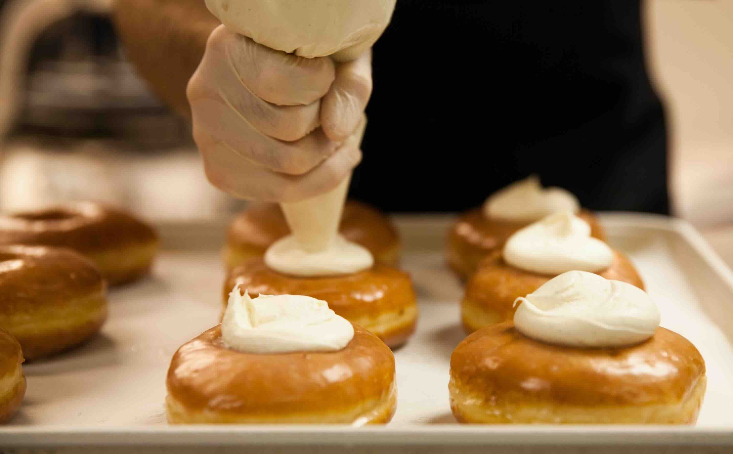 Chef pipping icing onto donuts.