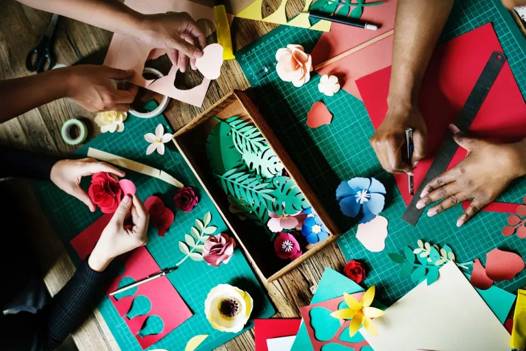 Hands working on paper crafts on a table. 