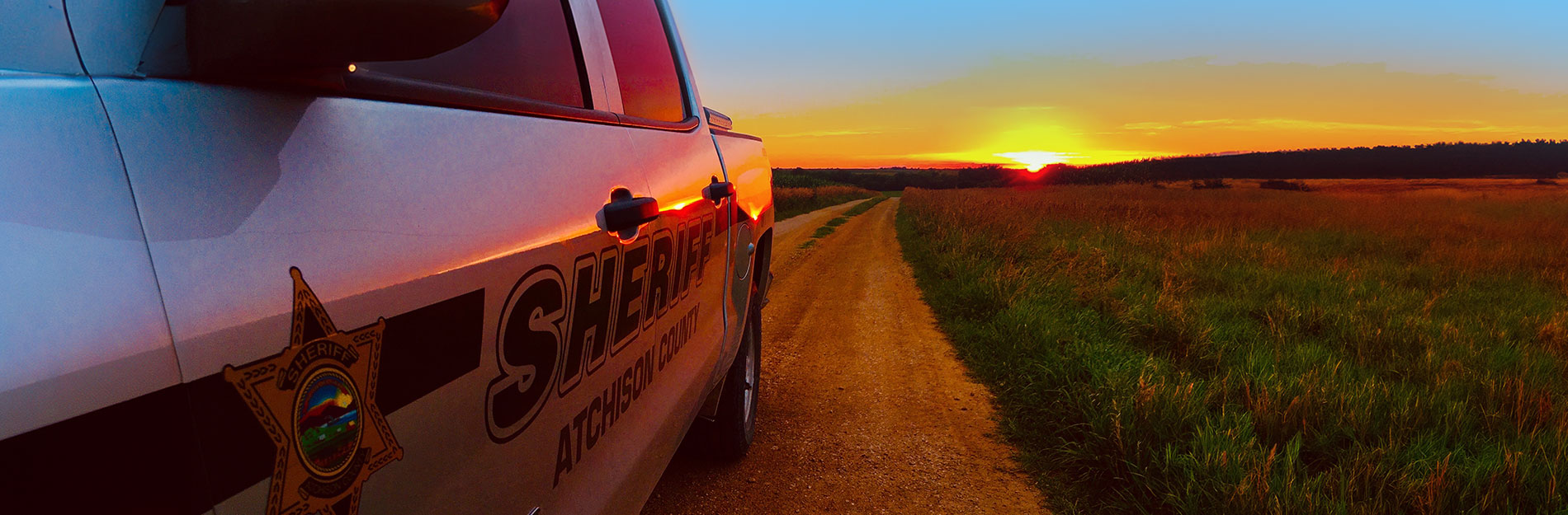Atchison County Sheriff truck on a gravel road between two fields at sunset.