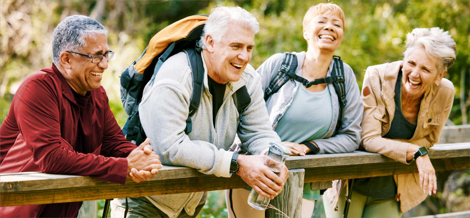 Group of 4 seniors leaning over a wooden balcony with 2 wearing hiking backpacks